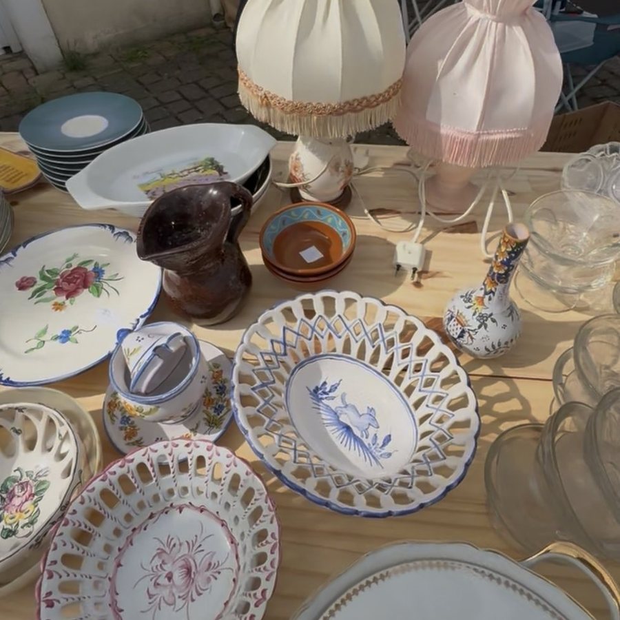 Une table de vide-grenier : vaisselle ancienne, pichet, lampes à franges